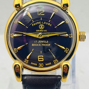 Könnte beinhalten: Eine goldfarbene Armbanduhr mit einem dunkelvioletten, strukturierten Zifferblatt, goldenen Zeigern und Indizes. Das Zifferblatt zeigt den Text Favre-Leuba Geneve, 17 Jewels, Shock Proof und Swiss Made. Sie hat ein dunkles Lederarmband und eine goldene Krone.