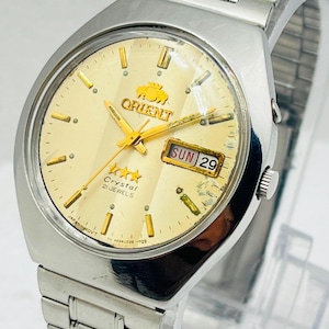Può includere: Un orologio da polso in acciaio inossidabile color argento con quadrante rotondo color champagne. L'orologio presenta lancette e indici dorati, una finestrella giorno-data che mostra SUN 29, il logo Orient con tre stelle e Crystal 21 JEWELS.