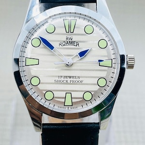 Op de afbeelding: Zilverkleurig RW Roamer horloge met een zwarte leren band. De wijzerplaat heeft een lichte achtergrond met groene en blauwe accenten. De tekst "17 JEWELS SHOCK PROOF" is zichtbaar.