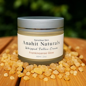 Op de afbeelding: Een pot Anahit Naturals Whipped Tallow Cream voor de gevoelige huid, met Frankincense Glow. De pot is omgeven door kleine, amberkleurige harsstukjes. Het etiket geeft 60 ml crème aan.