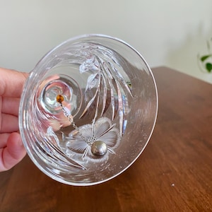 May include: Clear glass bell with etched floral and leaf designs. A small silver ball hangs inside the bell, suspended by a delicate chain. A small amber-colored bead is at the top of the chain.