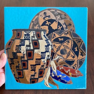 May include: A ceramic tile featuring a Southwestern design. The tile has a turquoise background with a brown and tan vase, two circular designs, and three colorful corn husks. The vase has a geometric pattern.