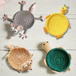 Puede incluir: Cuatro posavasos de ganchillo hechos a mano con forma de animales. Un ratón gris, un pato amarillo, una ardilla marrón y una tortuga verde. Cada posavasos es redondo con las características y extremidades del animal.