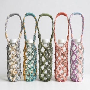 Puede incluir: Cinco portabotellas de agua de macramé coloridos. Cada soporte tiene una combinación de colores diferente, que incluye gris, verde azulado, verde oliva, coral y lavanda. Los soportes están diseñados para transportar una botella de agua transparente con una tapa blanca.