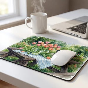 May include: A rectangular mouse pad featuring a watercolor illustration of a bouquet of pink and orange tulips in a glass vase, set on a wooden picnic table covered with a light blue and white checkered cloth, surrounded by lush green foliage.