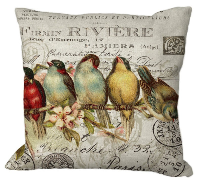 Puede incluir: Coj&iacute;n cuadrado con un dise&ntilde;o vintage que presenta cinco p&aacute;jaros coloridos posados en una rama con flores. El fondo tiene texto y sellos descoloridos, con el texto "FIRMIN RIVIERE" visible.