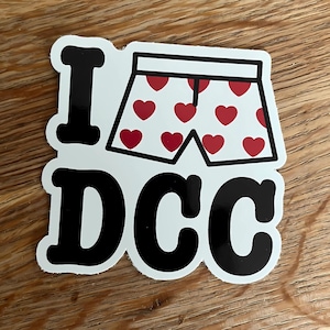 May include: A white sticker with the text "I DCC" in a bold, black font. Above the text is a cartoon image of white boxer shorts with red heart patterns.