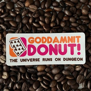 May include: A sticker with the text "GODDAMNIT DONUT!" in orange and pink, with a donut graphic, and the phrase "THE UNIVERSE RUNS ON DUNGEON" on a bed of coffee beans. The sticker is rectangular.