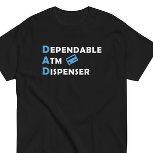 May include: Black t-shirt with the text "Dependable DAD ATM Dispenser" in white and blue. The ATM is represented by a blue credit card icon. The shirt is a short-sleeved crew neck.