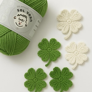 Op de afbeelding: Een bol groen garen en klaverblaadjes in groen en crème. Het garenlabel luidt "We provide, you ask... SOL YARN". De klavers zijn gehaakt.