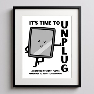 May include: A framed print with a black border. The artwork features a cartoon tablet with arms and legs, smiling and pointing towards the word "UNPLUG". Text reads "IT'S TIME TO" and "...FROM THE INTERENT. PLEASE REMEMBER TO PLUG YOUR IPAD IN!"