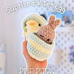 Könnte beinhalten: Ein gehäkeltes Osterei mit einem gelben Küken mit hellgrüner Kapuze und einem braunen Hasen, der herauslugt. Das Ei ist hellgrün und gelb. Der Text auf dem Bild lautet "Surprise Easter Egg" und "PDF Pattern."