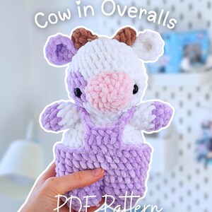 Könnte beinhalten: Handgemachtes Kuscheltier, eine Kuh mit lila Latzhose. Die Kuh ist weiß mit lila und braunen Akzenten, einer rosa Nase und schwarzen Augen. Der Text auf dem Bild lautet "Cow in Overalls" und "PDF Pattern".