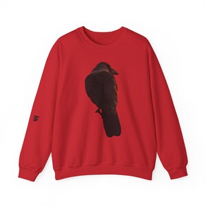 Peut inclure: Sweat-shirt rouge avec une illustration détaillée d'un corbeau noir. Le corbeau est perché, de dos. Un petit graphisme stylisé est sur la manche gauche. Un haut confortable et décontracté.