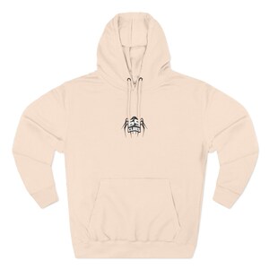 Peut inclure: Un sweat à capuche beige clair avec une poche avant et une capuche à cordon. Le sweat à capuche présente un graphisme noir sur la poitrine qui se lit "ASS CLUBS". Le sweat est fait d'une matière douce.