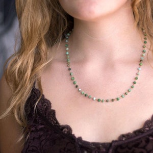 May include: A delicate necklace with small, round green gemstones and gold accents. The necklace is worn by a person with long, wavy hair.