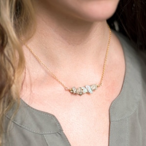 May include: A gold chain necklace with a cluster of small, irregular, light green and gray stones.