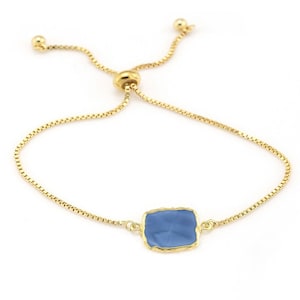 May include: A gold chain bracelet with a blue square-shaped gemstone pendant. The bracelet has an adjustable sliding clasp.