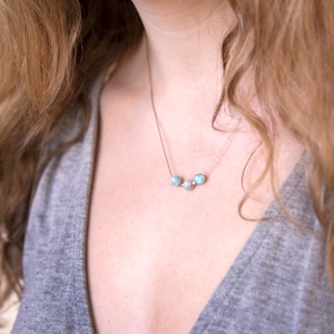 Pu&ograve; includere: Una collana a catena d'argento con tre perle di pietra preziosa blu chiaro.
