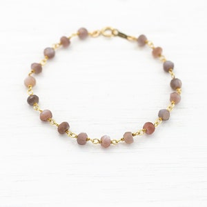 May include: A delicate gold chain bracelet with small, faceted, light pink and gray gemstone beads.