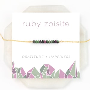 May include: A gold chain necklace with a bar of green and pink ruby zoisite stones. The card reads "ruby zoisite" and "gratitude + happiness".