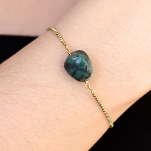 Puede incluir: Un brazalete de cadena dorada con un colgante de piedra preciosa verde. El brazalete tiene un cierre deslizante ajustable.