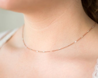 May include: A delicate rose gold chain necklace with a minimalist design. The chain is made of small, rectangular links.
