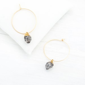 May include: A pair of gold hoop earrings with a gray crystal pendant on each earring.
