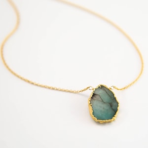 May include: A gold chain necklace with a large, irregular-shaped, teal green gemstone pendant. The pendant is outlined in gold.