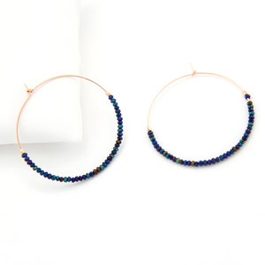 May include: A pair of hoop earrings with a thin gold wire frame and a row of iridescent blue beads.