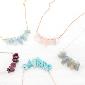 May include: Five necklaces with different colored gemstone pendants. Each necklace features a row of small, irregular shaped gemstones in a graduated size. The gemstones are aquamarine, rose quartz, turquoise, labradorite, and ruby.