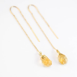 Puede incluir: Un par de pendientes de cadena dorada con piedras de citrino amarillo en bruto que cuelgan de los extremos.
