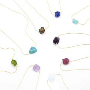 May include: Ten delicate gold necklaces with various natural stone pendants. Each necklace features a different color and type of stone, including turquoise, amethyst, lapis lazuli, and pyrite.