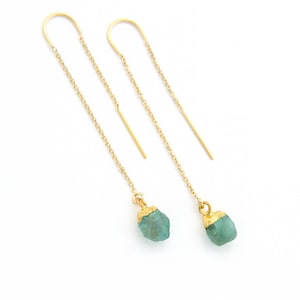 Puede incluir: Un par de pendientes de cadena dorada con gotas de piedras preciosas verdes. Las piedras preciosas son en bruto y tienen una textura natural rugosa.