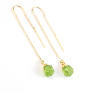 Op de afbeelding: Een paar gouden kettingoorbellen met groene edelsteen druppels. De oorbellen zijn lang en hangen van de oorlel.