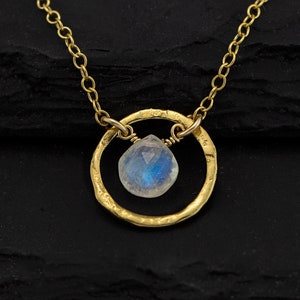 May include: A gold necklace with a delicate chain and a circle pendant featuring a moonstone gemstone.