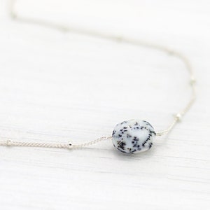 May include: A silver chain necklace with a single, round, white and black speckled stone pendant.
