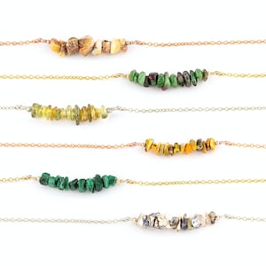Puede incluir: Cinco delicados collares con diferentes chips de piedras preciosas de colores. Cada collar presenta una cadena de oro o plata con un pequeño grupo de chips en una variedad de colores, incluyendo verde, marrón, amarillo y gris.