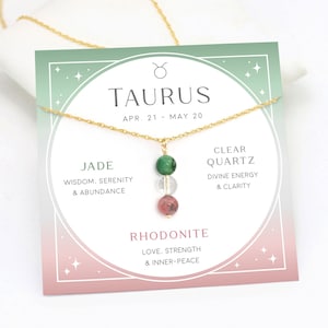 May include: A gold chain necklace with a pendant featuring three gemstone beads: green jade, clear quartz, and pink rhodonite. The card below the necklace reads "Taurus, Apr. 21 - May 20" and lists the properties of each gemstone.