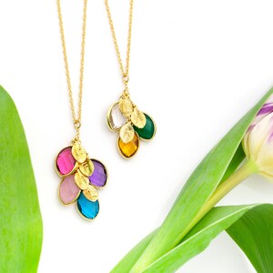 May include: Two gold necklaces with colorful gemstone pendants. The necklaces feature multiple small gold leaves and are displayed against a white background with a green leaf.