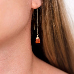 Puede incluir: Pendientes de cadena de oro con un pequeño colgante de piedra de cornalina naranja.