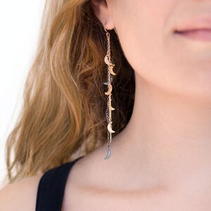 May include: A long, dangling earring with a chain of crescent moon charms. The charms are alternating gold and black.