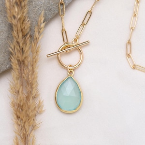 Op de afbeelding: Een gouden ketting met een toggle sluiting en een traanvormige lichtblauwe edelsteen hanger.