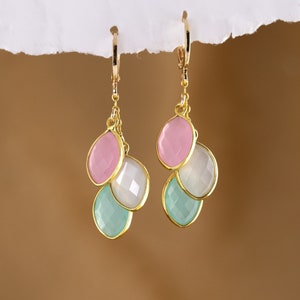 May include: Gold dangle earrings with three teardrop-shaped stones. The stones are pink, white, and light blue.