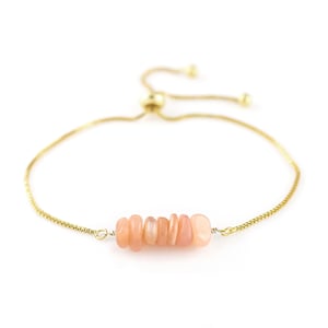 May include: A delicate gold chain bracelet with a cluster of light pink sunstone beads. The bracelet is adjustable with a sliding knot.