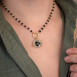 Peut inclure: Un collier en chaîne d'onyx noir avec un pendentif en or représentant un globe noir et blanc avec des étoiles et un anneau en or autour. Le collier mesure 40,6 cm de long.