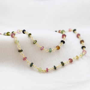 May include: A gold chain necklace with small, multi-colored gemstones. The gemstones are in shades of pink, green, black, and brown.