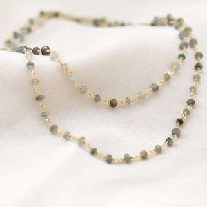 Peut inclure: Un collier délicat en chaîne dorée avec de petites perles de pierres précieuses bleu clair et grises.