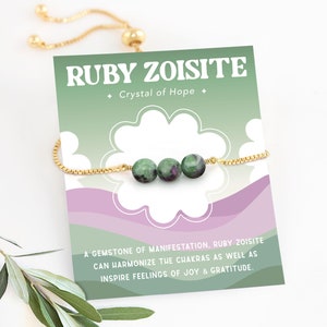 May include: A gold chain bracelet with three green and pink ruby zoisite beads. The bracelet is on a card that says "Ruby Zoisite + Crystal of Hope +" and "A gemstone of manifestation, ruby zoisite can harmonize the chakras as well as inspire feelings of joy & gratitude."