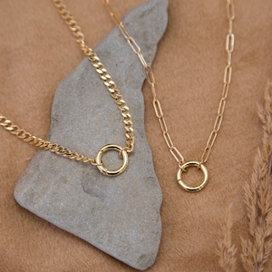 Puede incluir: Dos collares de oro con un colgante circular en cada uno. Los collares están sobre una superficie marrón claro con una roca gris.